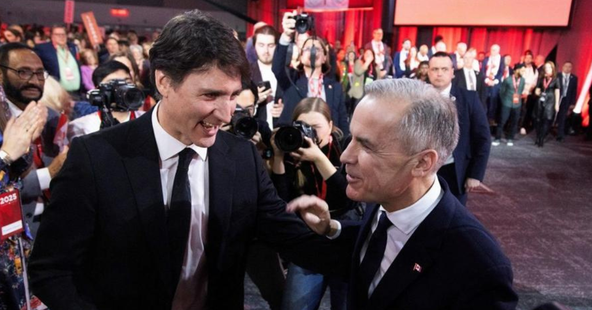 Justin Trudeau and Mark Carney smiling and shaking hands at a political event, surrounded by a crowd and press photographers with red lighting in the background.
